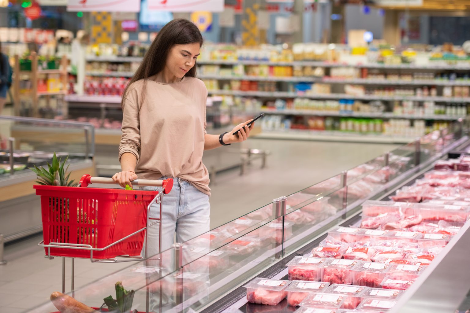 1654875326-stock-photo-young-woman-standing-in-aisle-with-shopping-cart-choosing-fresh-raw-meat-in-modern-supermarket-1808551621-1536x1024
