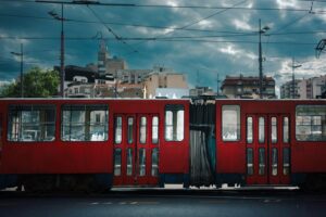 Empty red tram passing by, city surroundings on a cloudy and sunny spring day.