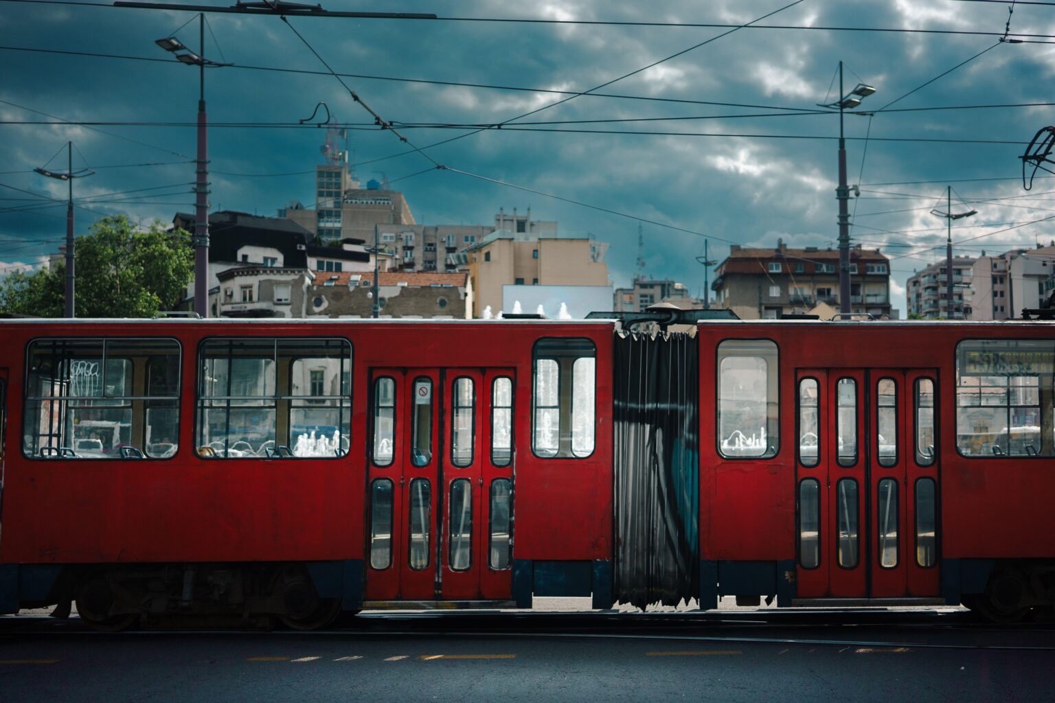 Empty red tram passing by, city surroundings on a cloudy and sunny spring day.